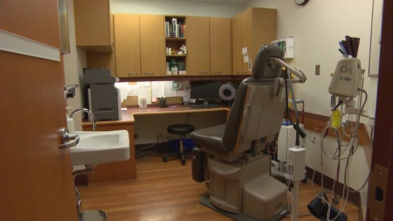 A hospital exam room with a large examination chair and other medical equipment is shown.