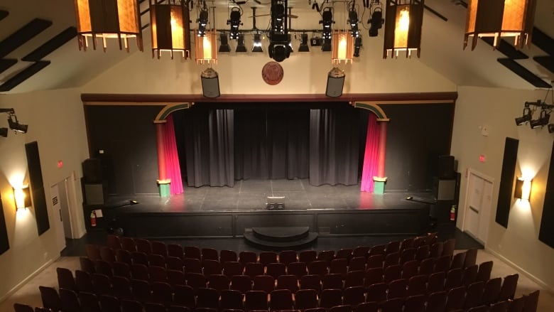 A birds-eye view of a theatre with rows of chairs and a black stage at the front.