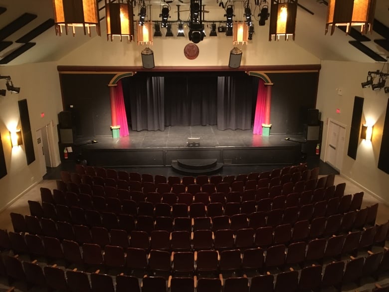 A birds-eye view of a theatre with rows of chairs and a black stage at the front.