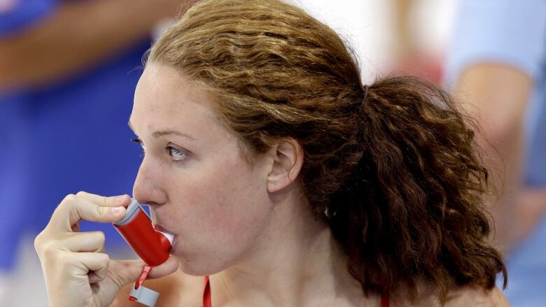 A woman wearing a bathing suit uses an inhaler. 