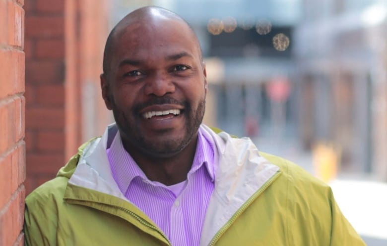 Moise is shown smiling, leaning on a brick wall.