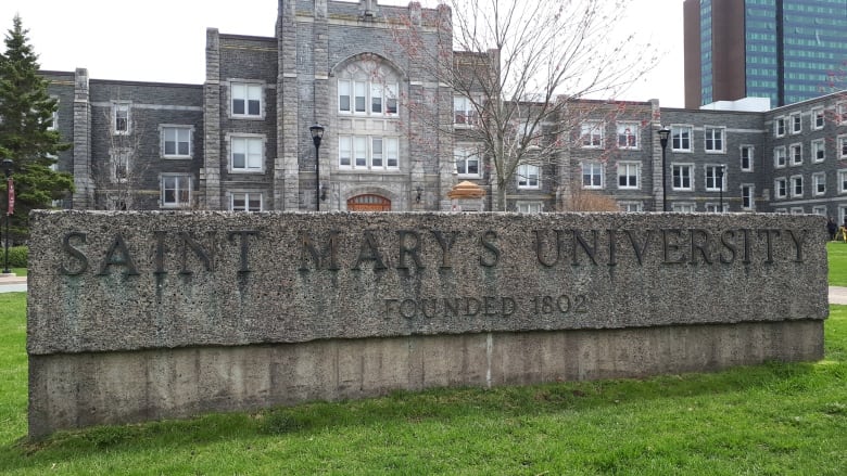 A large stone university building stands behind a large concrete sign for Saint Mary's University. 