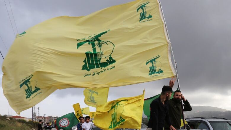 Large yellow and green flags wave from a line of cars, driving through an arid landscape. 