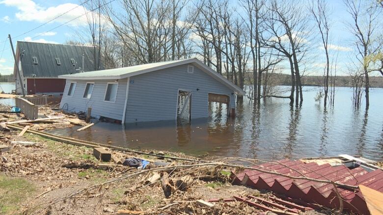 Two homes submerged in water with wood and debris surrounding them in the water and on land.