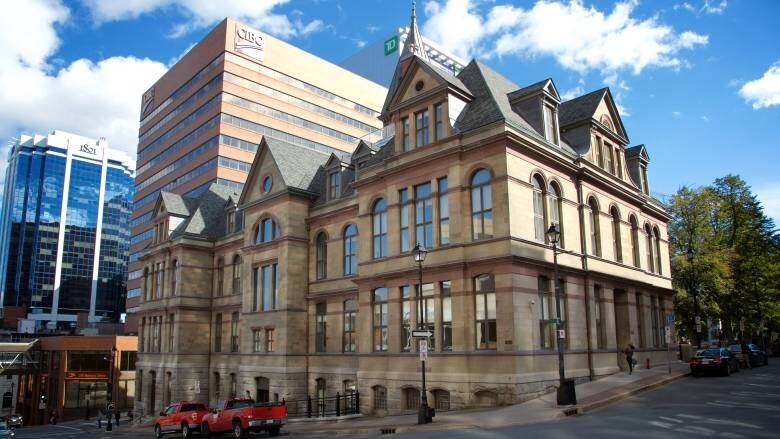 A view of Halifax city hall looking up at the large beige turreted building surrounding by large commerical buildings