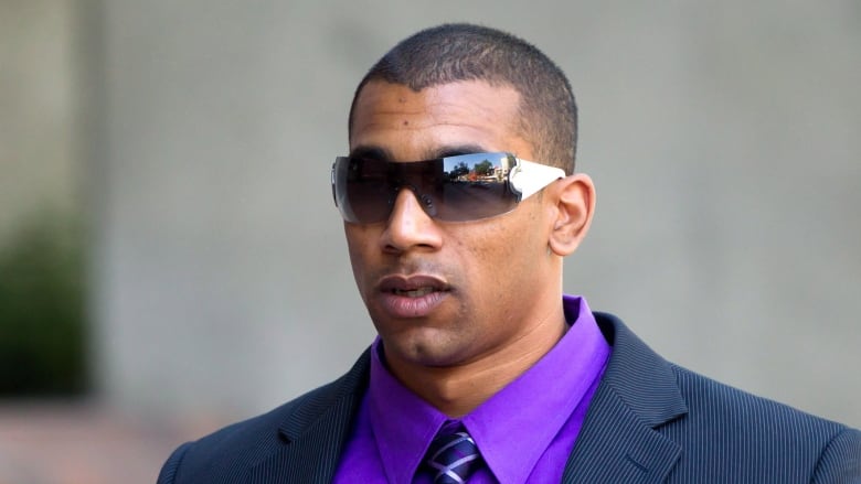 Josh Boden wears wraparound sunglasses, a navy blue suit and a purple shirt outside a Vancouver court.