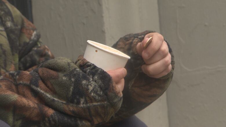 A close up photo of a person holding a cup and a loonie. 