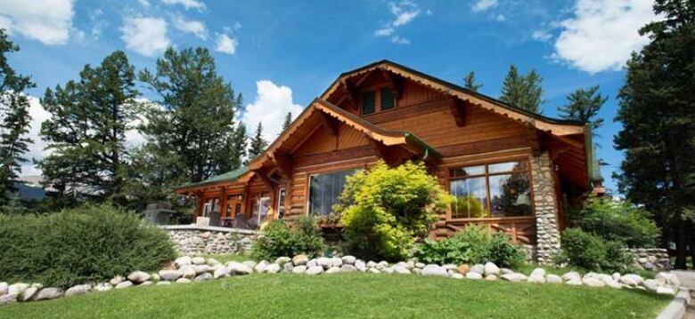 A warmly-coloured wood cabin surrounded by foliage on a sunny day