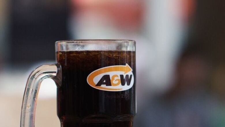 A glass mug, branded with an A & W logo sits on a counter, it is full of rootbeer