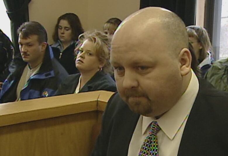 A man in black suit sitting in a court room. 