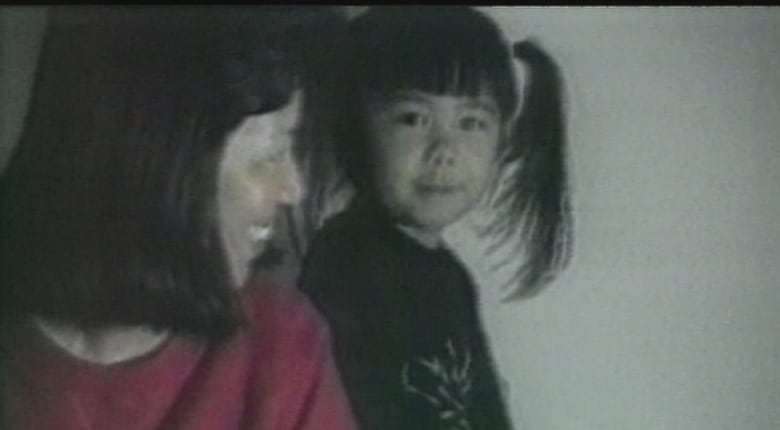 An East Asian woman smiles at her daughter, who has two ponytails.