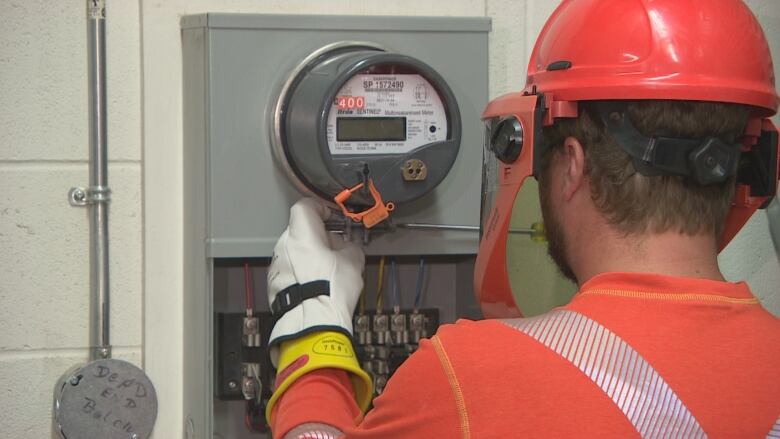 An electrical worker in a bright orange shirt and hardhat installs a smart meter.