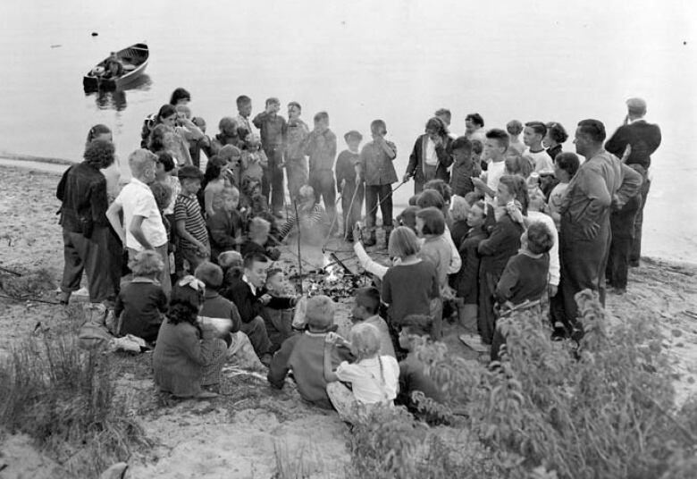 Large group of young people surround a campfire on a beach