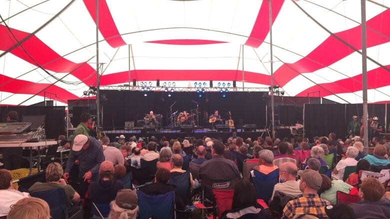 A crowd watches a band on stage inside a festival tent.