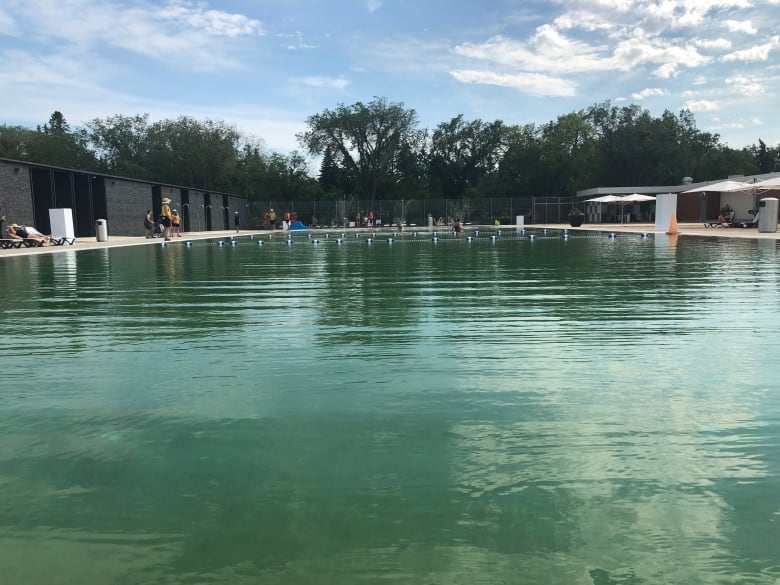 A lifeguard stands beside a pool filed with blue green water.