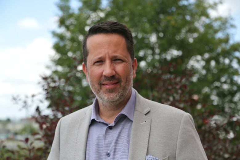 A man in a white blazer and purple shirt is shown.