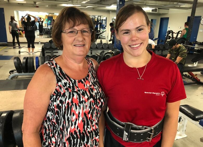 Two woman stand next to each other in a powerlifting gym.