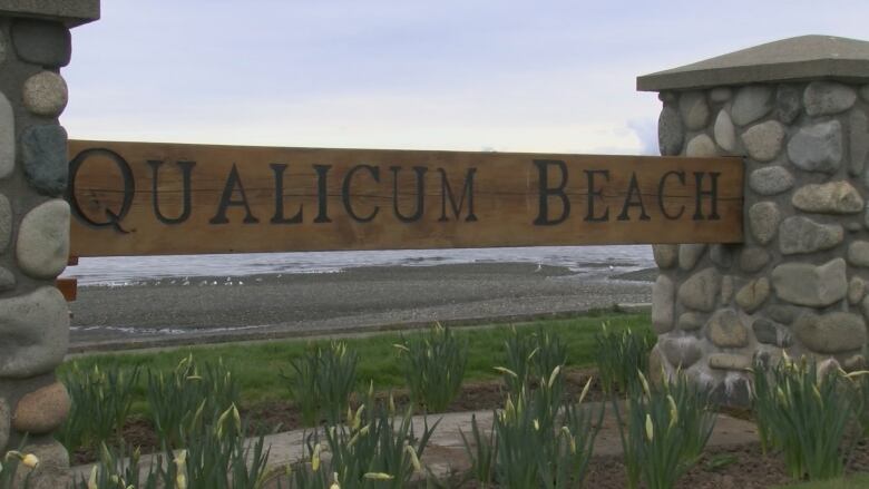 A sign that reads 'Qualicum Beach' next to a beach.