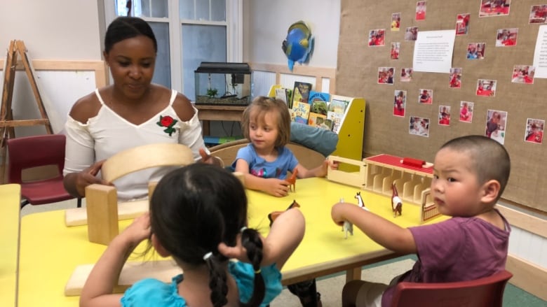 A Black adult woman supervises toddlers at a table in a child-care centre.