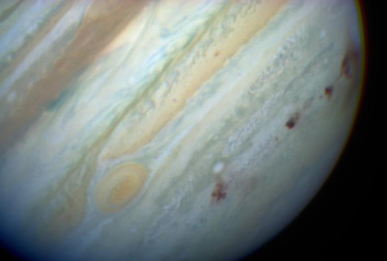 Jupiter's cloud bands are seen close-up with black spots.