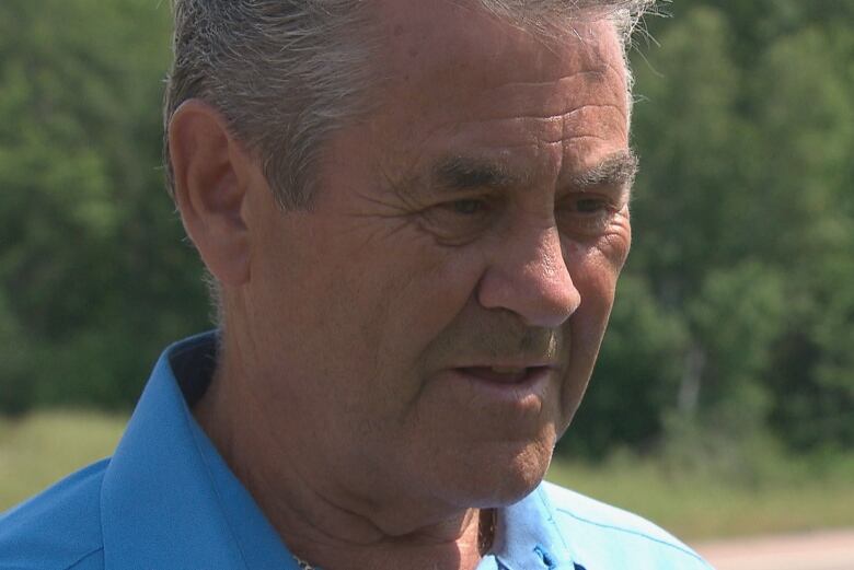 A close up of a man with short grey hair wearing a light blue collared shirt.