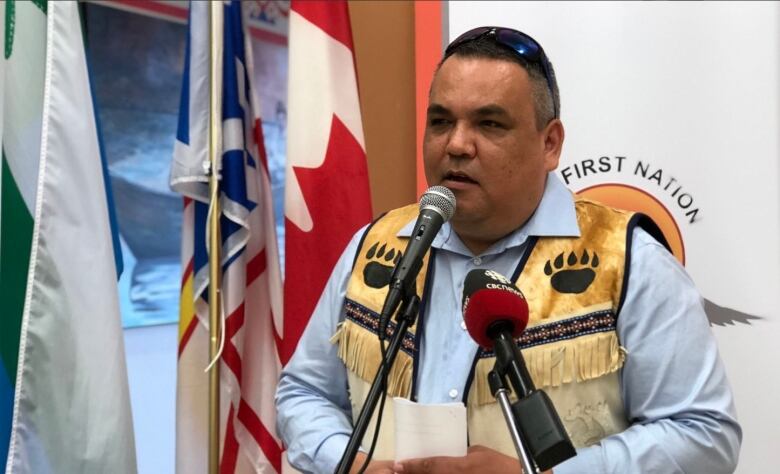 A man wearing a fur vest speaks at a podium.