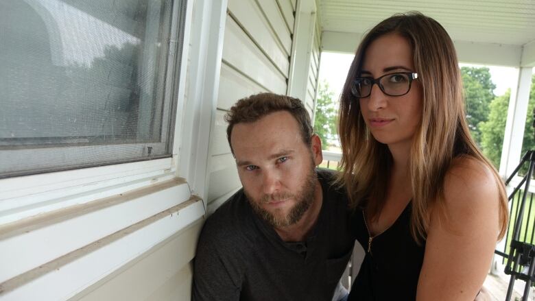 A man and woman stand on the outdoor deck of their home.