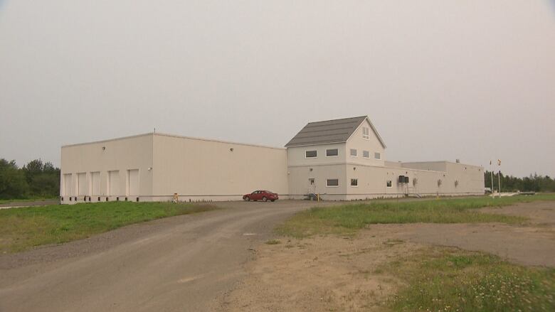 A large, white building with a lone vehicle parked in front of it. 