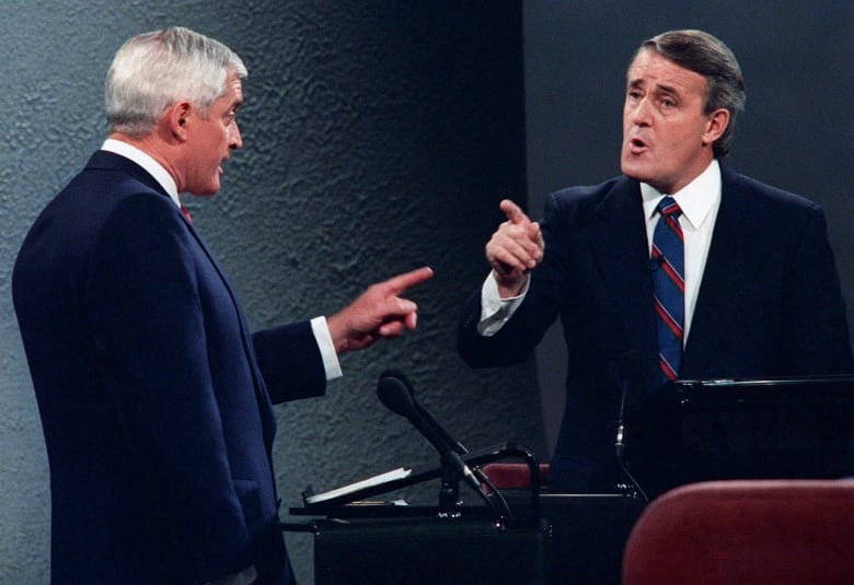 Two men at lecterns pointing at each other