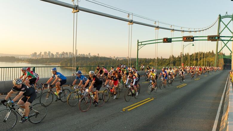 A peloton of cyclists bike down the bridge leading to Stanley Park.