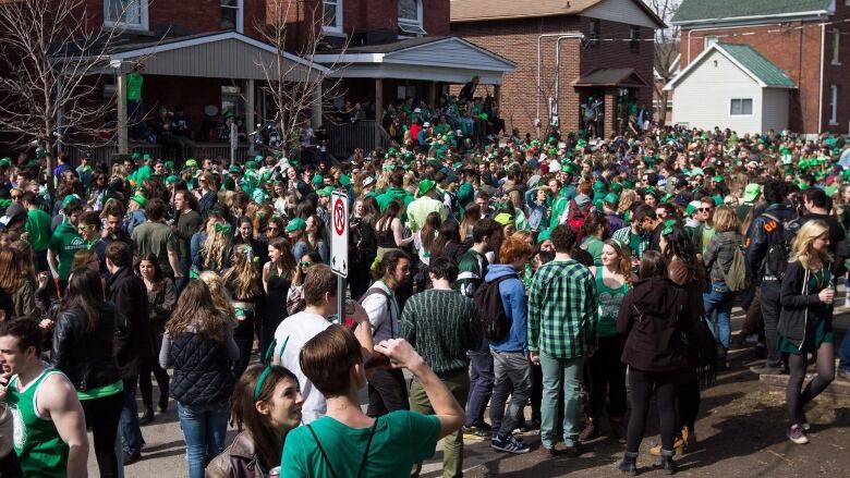 A big crowd of people wearing green clothes fill a city street. There are other people crowding on porches and sitting on railings all along the road.