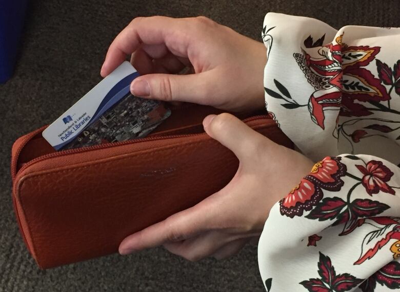 A woman's hand pulls a library card out of a red wallet.