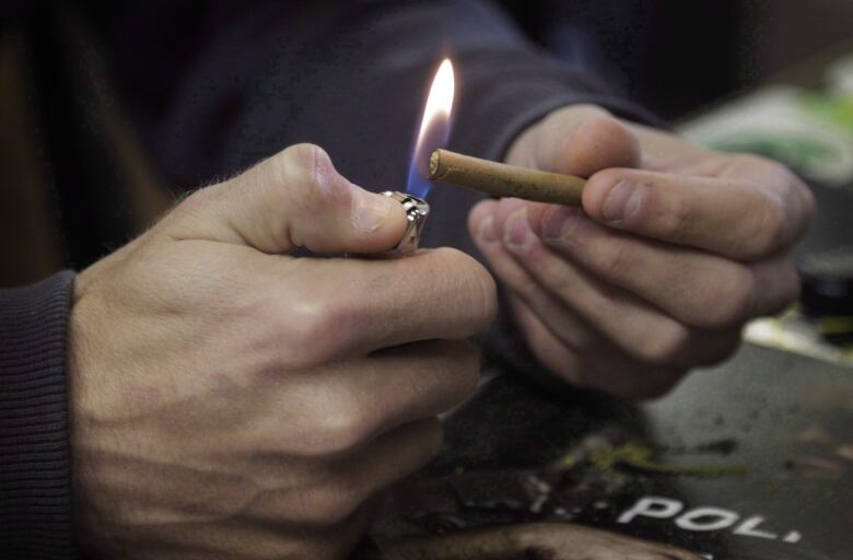 Fingers hold the end of a joint of marijuana under a flame.