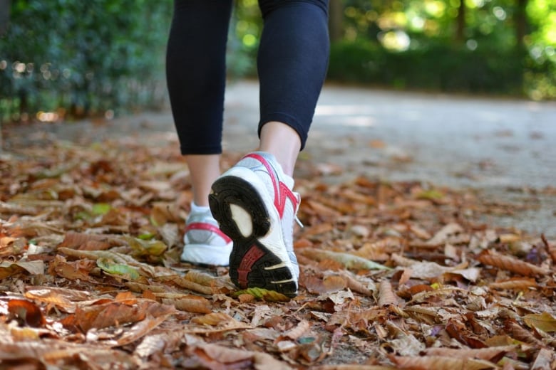 A woman's lower legs and feet are seen wearing leggings and running shoes and walking down a street where leaves have fallen.