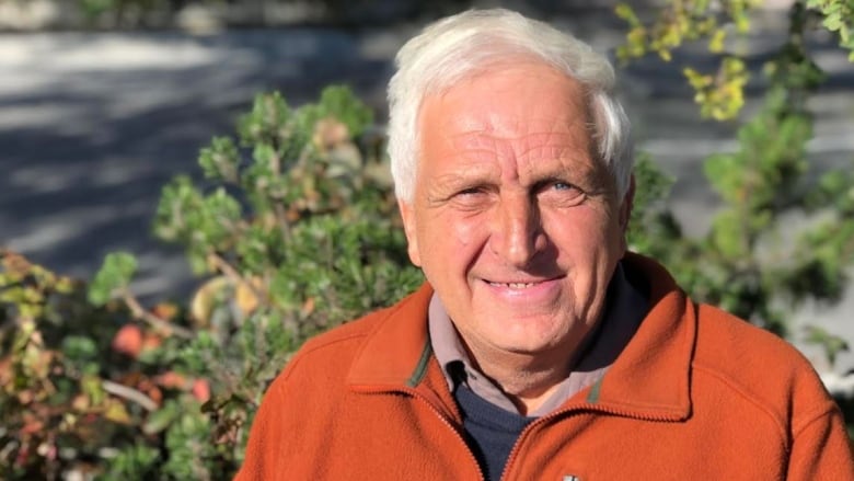 A man wearing an orange jacket with some trees in the background.