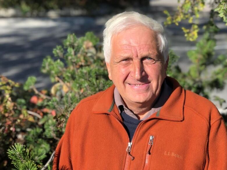 A man wearing an orange jacket with some trees in the background.