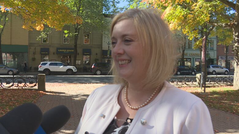 A woman stands outside on a busy sidewalk speaking into a microphone.