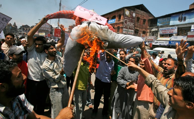 A crowd of protesters burns an effigy in the street.