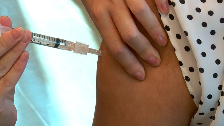 A health care  worker holding a needle is seen injecting a patient's arm with vaccine.