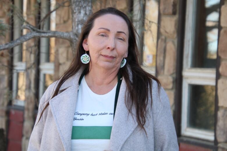 Chief Lynne Acoose stands for a portrait outside while wearing a grey jacket and a white and green shirt underneath