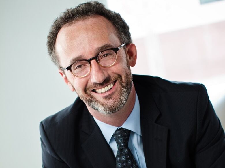 A bearded man in a suit wearing glasses.