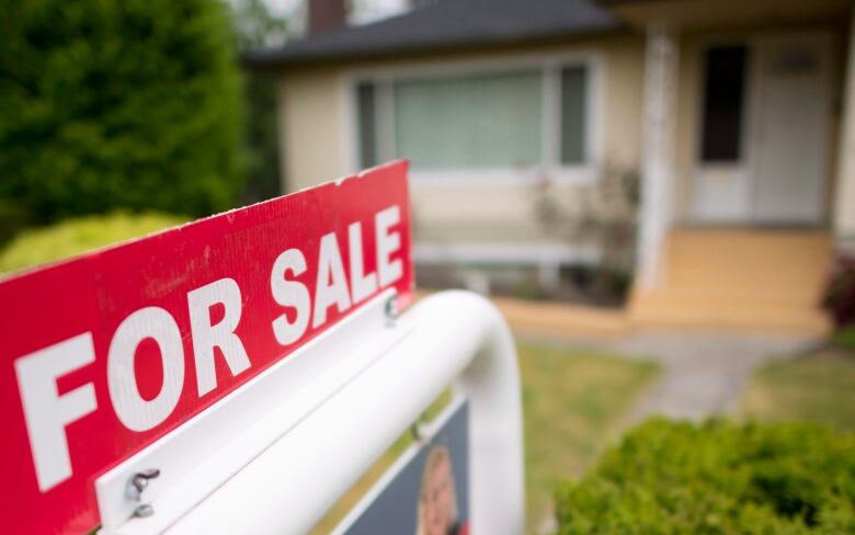 A large For Sale sign is seen in the foreground with a blurred-out house in the background.