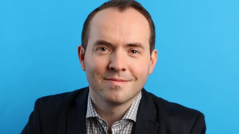 A man poses in front of a bright blue background