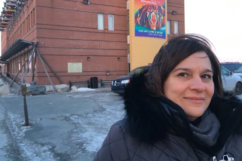 Woman stands infront of building in black coat.