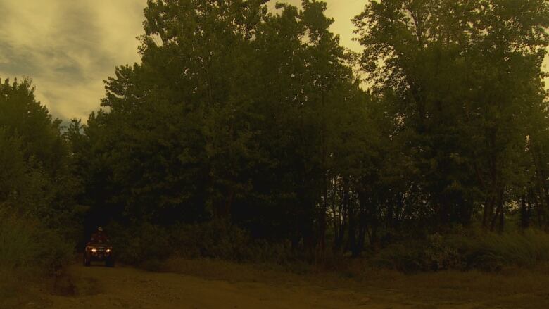 An ATV riding on a trail at dusk with its headlights on.