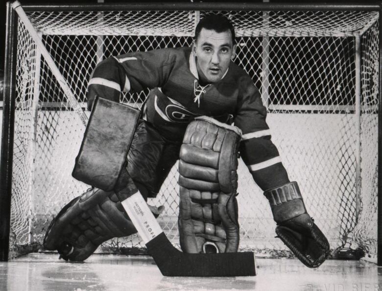 A goalie with full gear is in a defensive pose in front of a hockey net. 