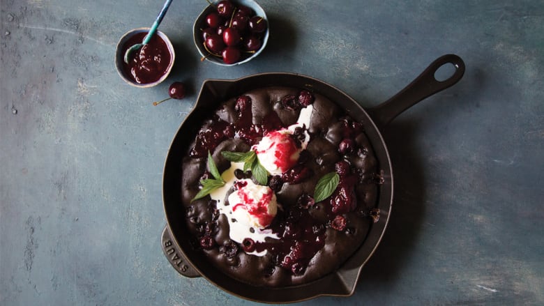 Overhead shot of brownies topped with vanilla ice cream and cherries in a cast iron skillet.