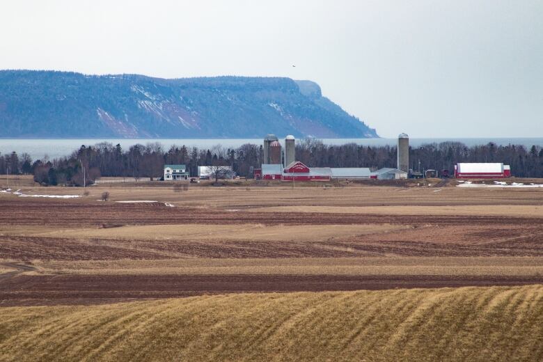 A farm in the foreground with a stretch of water and a hilly peninsula in the background.