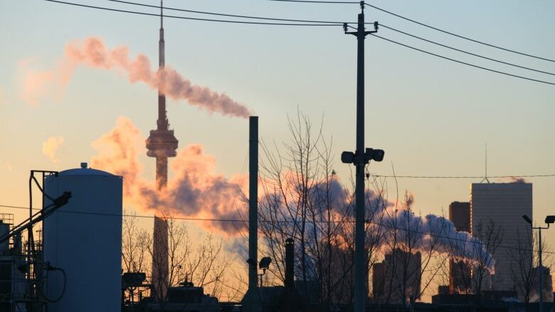 The city of Toronto skyline is framed by power lines, smoke stacks and petroleum storage tanks.