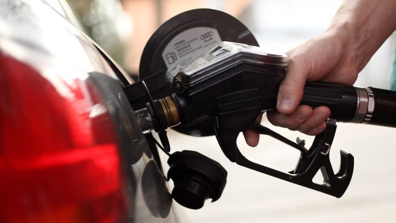 A hand holds a gas nozzle to fill a car's gas tank.